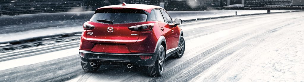 Mazda CX-3 rouge, vu de dos, un peu de biais, sur une route enneigée